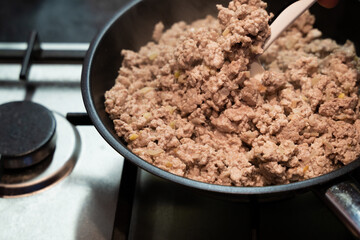 Frying minced meat with onions in a metal frying pan with non-stick coating on a stainless steel gas stove close-up top view copy space.