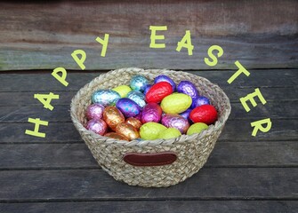 Basket with chocolate Easter eggs on a wooden table , text'Happy Easter'.