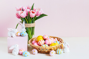 Fototapeta na wymiar Pink tulips, easter bunnies with colorful eggs in basket.