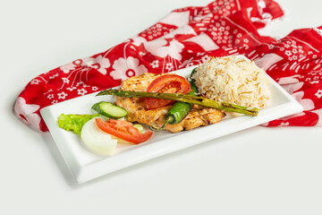 Grilled Chicken Breast with rice, tomato, cucumber in a dish isolated on colorful table cloth top view on grey background