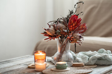 Cozy home composition with candles and protea bouquet.