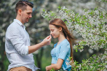 Adorable little girl with young father in blooming cherry garden on beautiful spring day