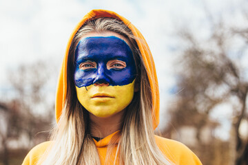 Outdoor portrait of young girl with blue and yellow ukrainian flag on her face