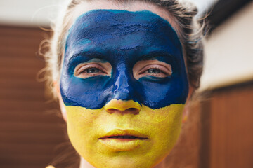 Outdoor portrait of young girl with blue and yellow ukrainian flag on her cheek