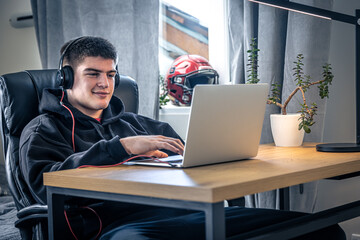 A young male athlete sits in front of a laptop in his room.