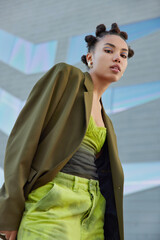 Fashionable woman with trendy hairstyle dressed in green fashionable clothes looks confidently at...