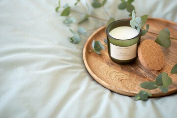 Green scented candle and a branch of eucalyptus on a wooden tray.