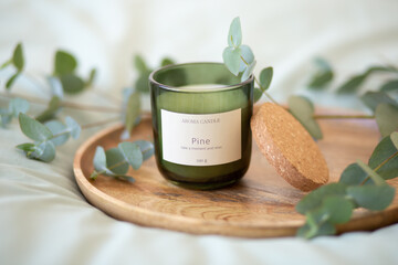 Green scented candle and a branch of eucalyptus on a wooden tray.