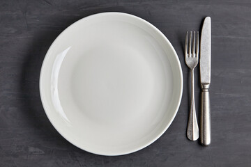 White plate on a dark concrete background with cutlery