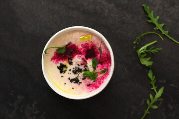 Cauliflower puree potato soup with arugula in round bowl on a black background, top view. Vegetarian healthy food delivery concept