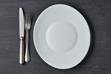Fototapeta na wymiar Oval white plate on a dark concrete background with cutlery