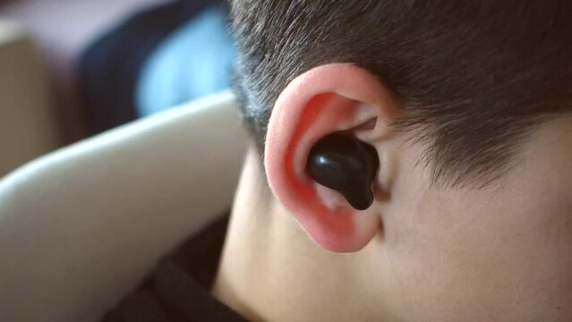 a teenager has a bluetooth headset in his ear and is listening to music, close-up earphones and ear,