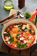 Shakshuka Homemade fried eggs poached in sauce of tomatoes, olive oil, peppers, onion and garlic in iron frying pan on old grey slate background. Traditional cuisine of Israel. Late breakfast concept