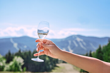 hand with glass of sparkling wine on mountains background