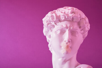 copy of the head of an antique statue of David with a taped mouth in pink neon light on a purple...