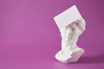 a copy of the head of an antique statue of David with a white empty blank plate on a purple...
