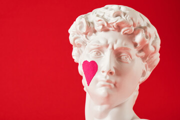 a copy of the head of an antique statue of David with a pink heart pasted on the cheek