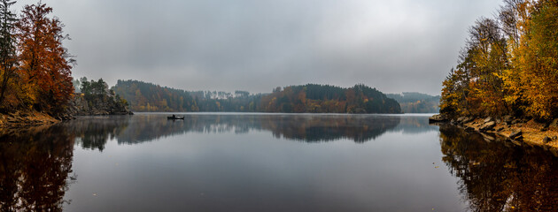Foggy Landscape With Fishermans Boat On Calm Lake And Autumnal Forest At Lake Ottenstein In Austria