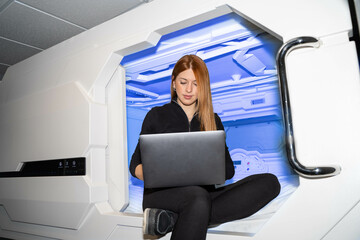 Digital nomad girl working with her laptop in a capsule hotel. 