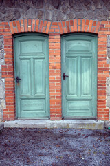 two old green wooden doors at building with brick wall