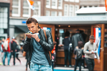 Happy caucasian tourist with fresh herring with onion and netherland flag in Amsterdam. Traditional dutch food outdoor