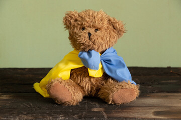 Teddy bear with the national flag of Ukraine on a wooden table at home,peace in Ukraine