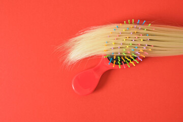 a strand of blond hair and a red plastic massage comb on a red background