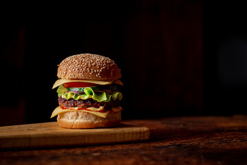 Hamburger day. Hamburger with grilled meat cheese, green salad and tomato. Wooden background. Place for text.