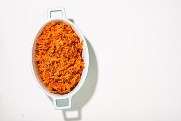 Jollof rice in a dish on a white background. Traditional Nigerian food made from rice, tomatoes and spices. Top view, place for text.