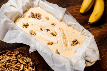 Banana bread. Cooking. Raw dough with banana and walnuts in a baking dish. Wooden background. Sweet, vegetarian food.