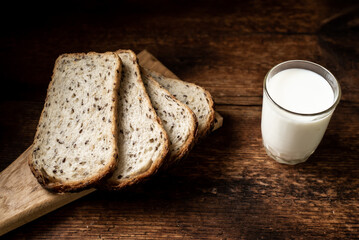 Pieces of bread with seeds and a glass of milk. Dark wooden background. Morning breakfast. Healthy food.