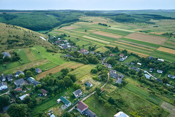 Fototapeta premium Aerial landscape view of green cultivated agricultural fields with growing crops and distant village houses