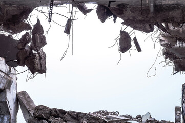 A hole in the body of a building with a pile of construction debris and concrete fragments hanging...