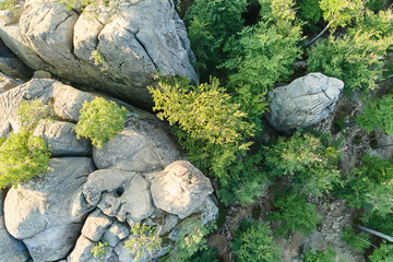 Aerial view of bright landscape with green forest trees and big rocky boulders between dense woods in summer. Beautiful scenery of wild woodland