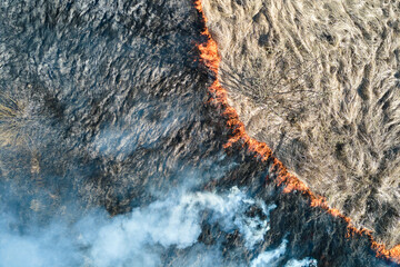 Aerial view of grassland field burning with red fire during dry season. Natural disaster and...