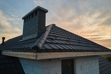 Chimney on house roof top covered with metallic shingles under construction. Tiled covering of building. Real estate development