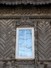 Carved architraves around the window of an old house. View of a fragment of the wall of a house with carved decorations around the window. - obrazy, fototapety, plakaty