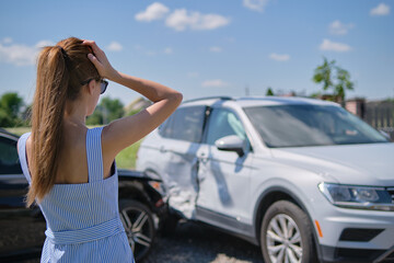 Fototapeta na wymiar Sad young woman driver standing near her smashed car looking shocked on crashed vehicles in road accident