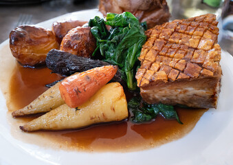 Roast pork Sunday lunch meal. The pork has crispy skin crackling. The vegetables are turnips and carrots with spinach and roast potatoes.