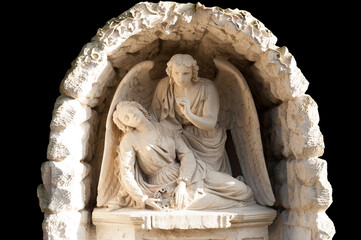 The stone sculpture of an angel supporting a sleeping girl isolated on the black background