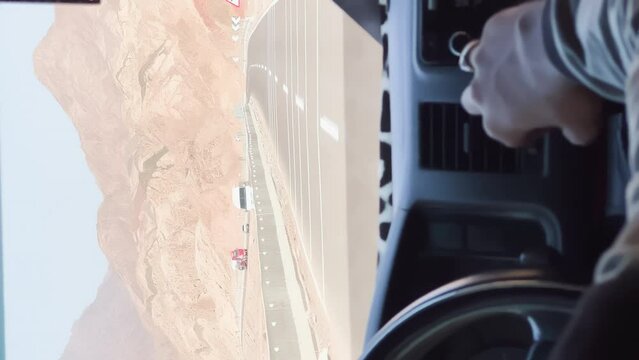 view from the cab of the car, the car is driving on the road in the desert, the hands of a man on the steering wheel of the car, mountainous terrain, cars in the oncoming lane of the road