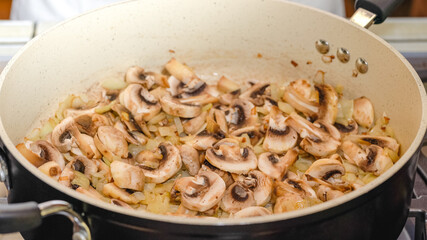 Chopped white mushrooms and chopped onion close up on frying pan.