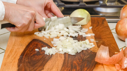 Chopping white onion on wooden chopping board on kitchen table. Close up cooking process