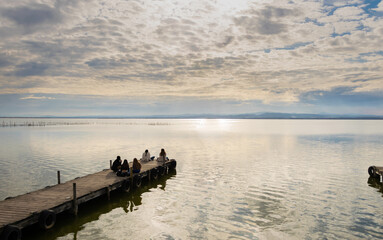 Fototapeta na wymiar vistas de la la albufera de valencia ,desde el puerto de puchol , donde se ve gente sentada en el muelle disfrutando del atardecer con un bonito cielo nublado .