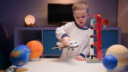 Little blonde boy kid plays with space shuttle from constructor, flies near planets of solar system...
