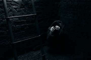 Fototapeta na wymiar A man hides in a bomb shelter covering their head with hands. The human sits on the floor in dungeon during shelling. Terrible conditions. Fear, danger, hunger and cold. Concept of wartime. Life save
