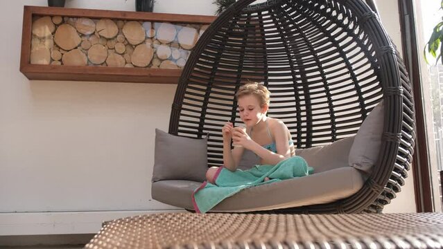 A teenage girl is happy to eat dessert from a cup. A child in a bathing suit is comfortably seated in a hanging chair. Child after swimming in the pool. Cozy and cute picture