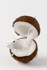 Halved coconut with milk splash on white background. Creative composition with coconut and milk.