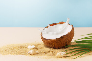 Halved coconut with milk splash on summer background with beach sand. Creative composition with...