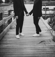 Fototapeta premium European Gay Couple holding hands, wearing black suits, wedding day of a same sex couple. Black and white art photography.